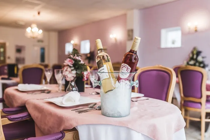 A dining table laid with a pink cloth, wine and purple chairs