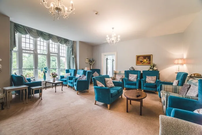 A wide view of the residents' lounge with blue seating and tall windows