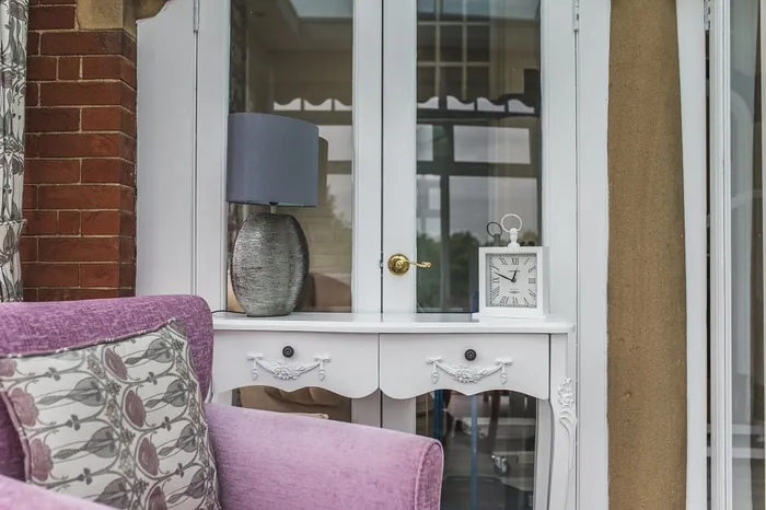 A pink armchair beside a white cabinet and table lamp