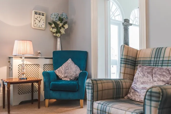 A teal armchair and a plaid wingback chair beside a garden window