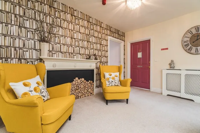 A lounge with two yellow armchairs in front of a fireplace and a red door