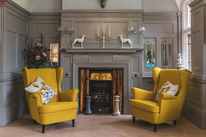 A residents' lounge with yellow armchairs either side of a marble fireplace